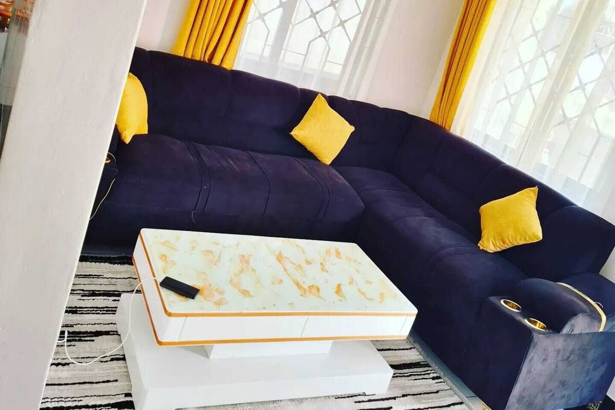 Un salon avec un canapé bleu foncé, des coussins jaunes, une table basse blanche et des rideaux jaunes.