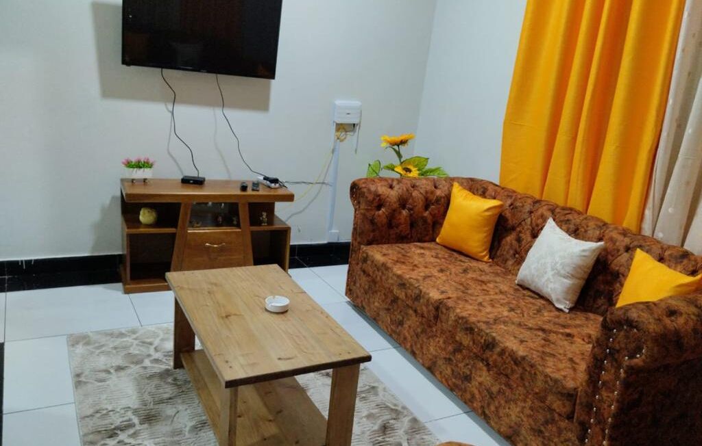 A living room with a sofa, a coffee table, a TV mounted on the wall, and a small wooden side table.