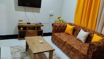 A living room with a sofa, a coffee table, a TV mounted on the wall, and a small wooden side table.
