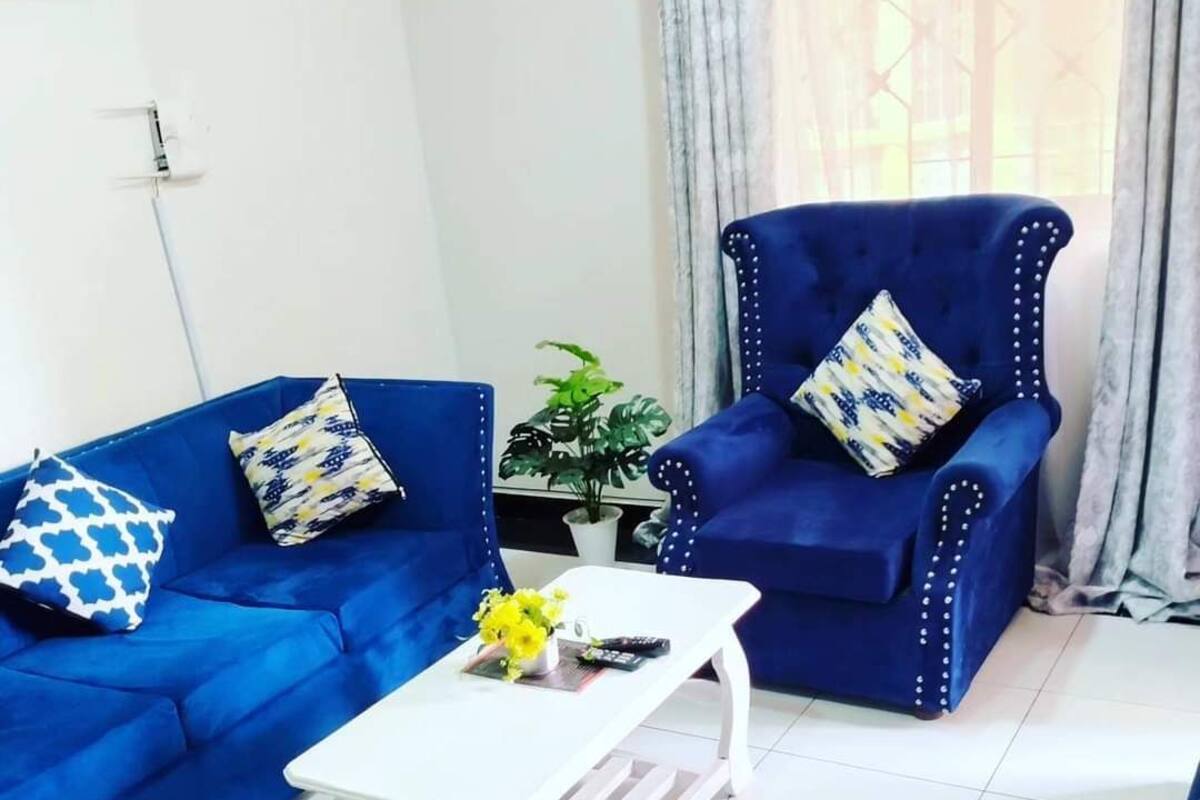 Un salon avec un canapé bleu, un fauteuil assorti et une table basse blanche sur laquelle est posé un vase de fleurs.