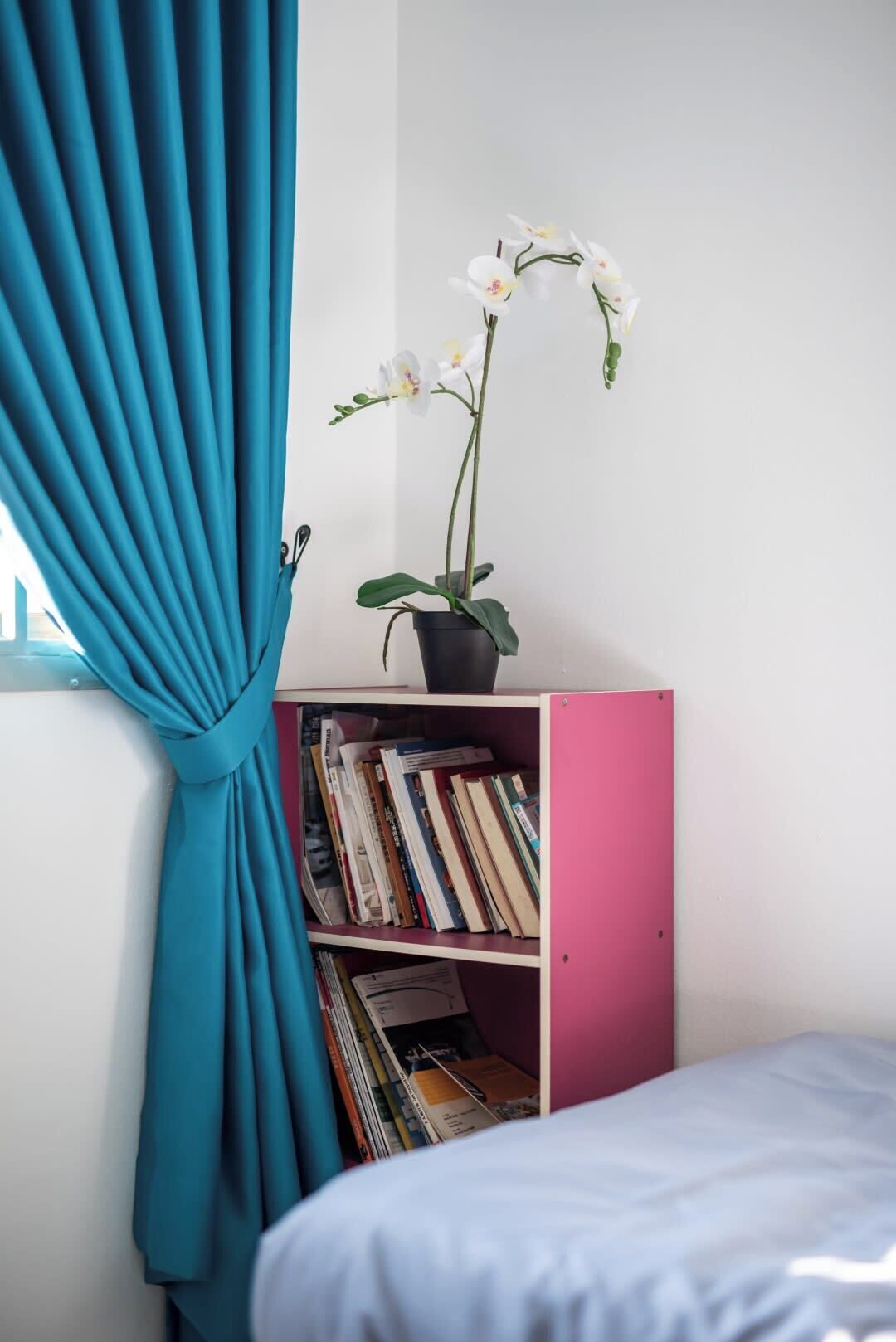 Une pièce avec des rideaux turquoise, une bibliothèque rose et un lit blanc.