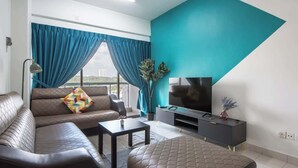 A modern living room with a sofa, a coffee table, a TV on a stand, and a large window with curtains. - Modern 3BR Near Danga Bay JB Free Parking (Johor Bahru)