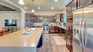 A modern kitchen with dark wood cabinets, stainless steel appliances, and a large island with a tray of food.