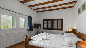 A bedroom with a wooden bed, a desk, a lamp, a window with curtains, and a view of greenery outside. - Pretty chalet-style studio (Euseigne)