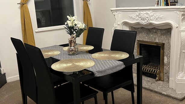 A dining area with a black table, four chairs, a vase with flowers, and a fireplace with books on the mantel.
