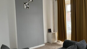 A modern living room with grey walls, a grey sofa, a small white cabinet, and a window with brown curtains.