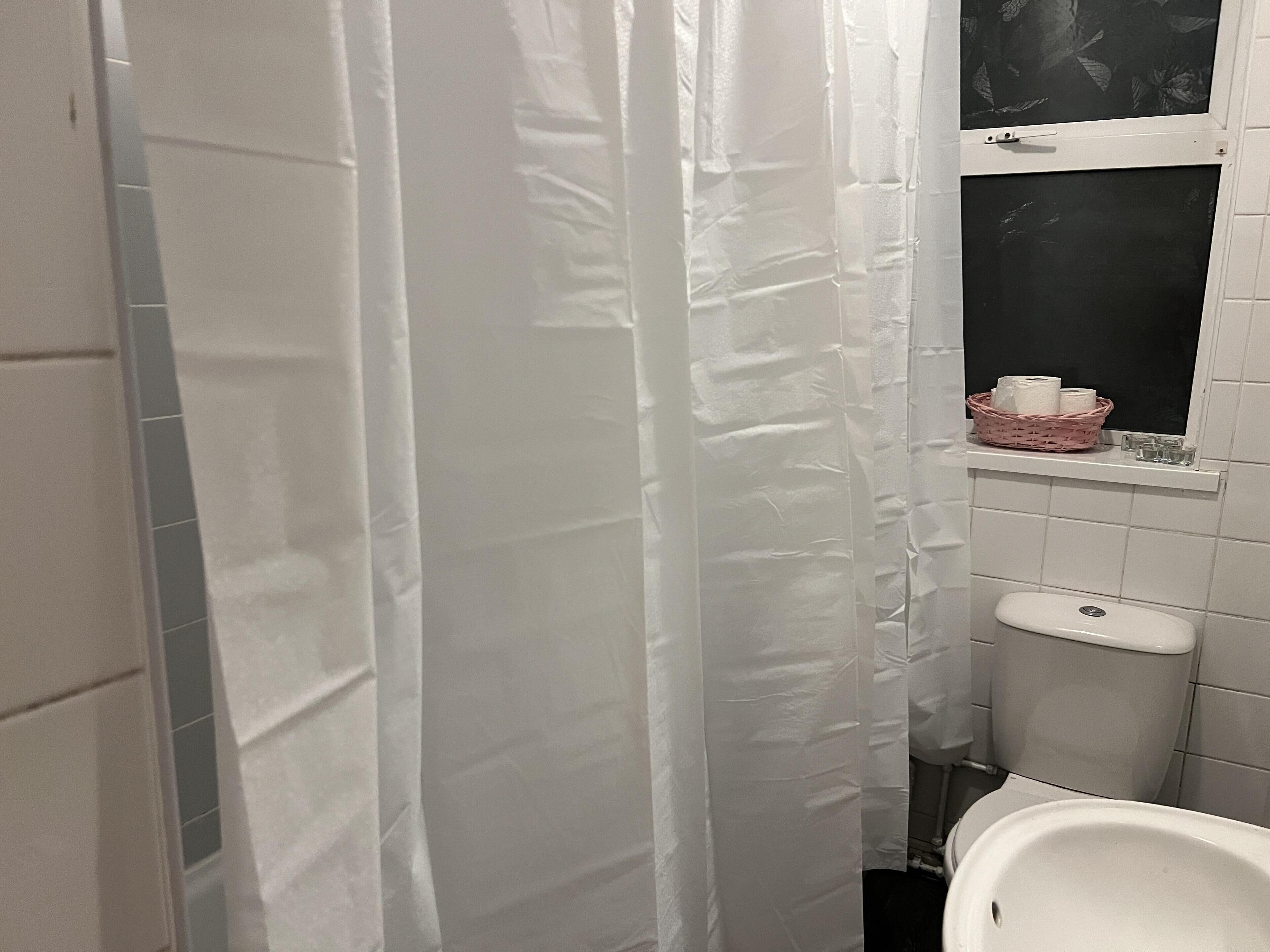 A bathroom with a white shower curtain, a white sink, and a window above the sink.