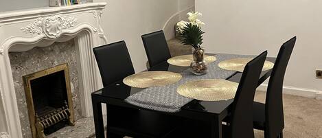 Een eettafel met zwarte stoelen, een witte schoorsteen en een vaas met witte bloemen.