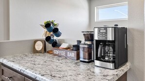 Uma cozinha com um cantinho de café, uma cafeteira e uma placa com a frase 'Our Little Coffee Bar'.