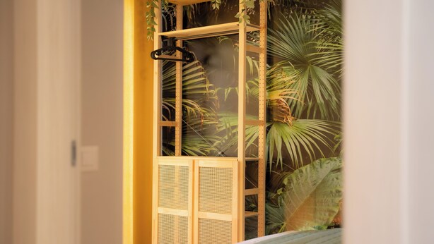 Ein Schlafzimmer mit einem Bett, einem Fenster mit Blick auf tropische Pflanzen und einem Holzschrank.
