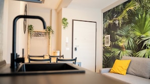 Eine moderne Küche mit einem schwarzen Wasserhahn, einem Esstisch mit Stühlen, einem grauen Sofa mit einem gelben Kissen und einer Tür mit einem an der Wand befestigten Telefon.