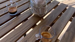 Ein Holztisch mit zwei Kaffeetassen und einem Glasbehälter voller Kaffeepäckchen auf einem Balkon.