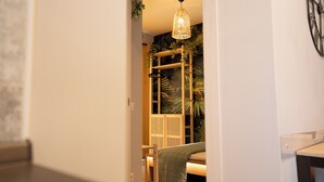 Ein Durchgang zu einem Raum mit einem Bett, einer Pendelleuchte sowie einer Wand mit Pflanze und Uhr.