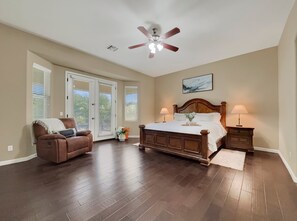 Une chambre avec un grand lit, un ventilateur de plafond, une chaise et une vue sur l’extérieur, visible à travers les portes.