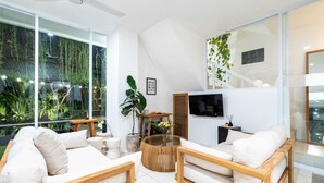 Un salon moderne avec un canapé, une table basse et un téléviseur. Une grande fenêtre offre une vue sur la verdure à l’extérieur.