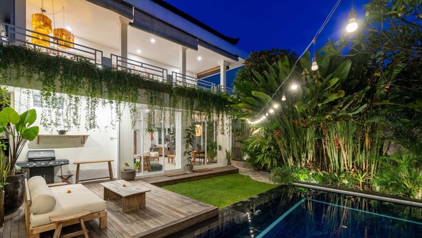 Un espace piscine extérieur moderne, doté d’une terrasse en bois, de chaises longues et d’un petit jardin.