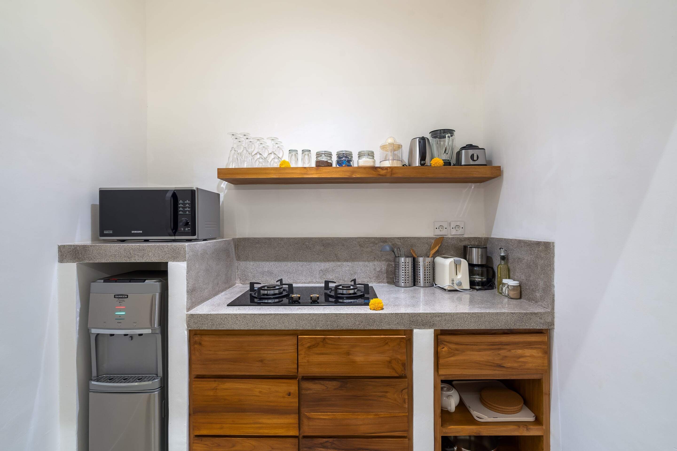 Una cocina compacta con microondas integrado, dispensador de agua, estufa a gas y cafetera.