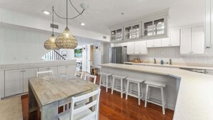 A modern kitchen with white cabinetry, a wooden dining table, and a bar area. - Ocean Front Oasis - Team Joseph Ellen (Jacksonville Beach)