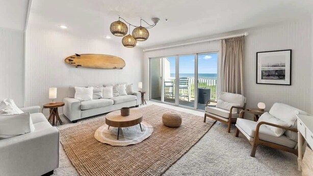 A modern living room with a sofa, chairs, a coffee table, and a large window with a view. - Ocean Front Oasis - Team Joseph Ellen (Jacksonville Beach)