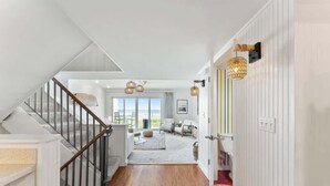 A staircase leading to a living area with a view, a wooden floor, and a light-colored wall. - Ocean Front Oasis - Team Joseph Ellen (Jacksonville Beach)