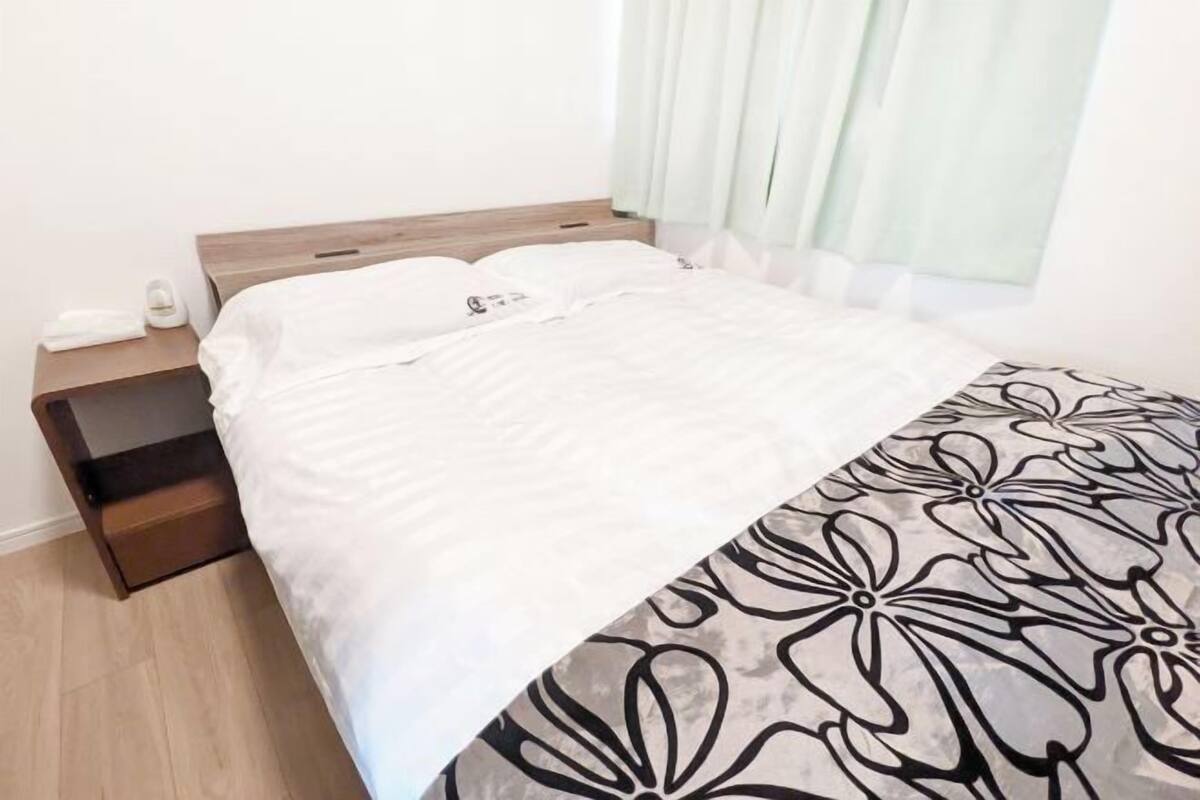 A neatly made bed with white bedding and a black and white floral throw blanket.