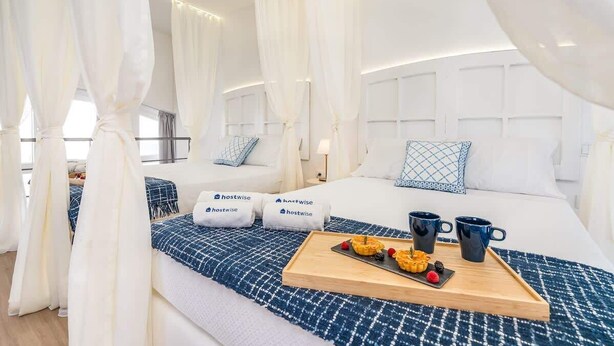 Ein Hotelzimmer mit einem großen Bett, weißen Vorhängen, einer Platte mit Gebäck und einer blau-weißen Decke.