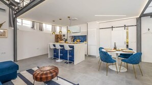 Eine moderne Küche mit einer zentralen Kochinsel, Barhocker und einem Essbereich mit rundem Tisch und blauen Stühlen.