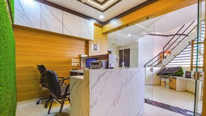 A reception area with a marble counter, wooden paneling, a black office chair, and a staircase in the background. - HOTEL GREEN TREE (Ahmedabad)