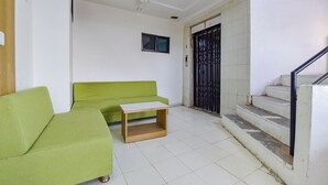 A room with a green sofa, a small wooden table, a ceiling fan, a window, and a staircase leading to an upper floor. - HOTEL GREEN TREE (Ahmedabad)