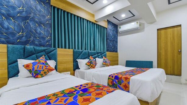 A hotel room with two beds, each with a colorful geometric-patterned bedspread. The room features a modern design with a blue and gold color scheme, a wooden headboard, and a large window with curtains. - HOTEL GREEN TREE (Ahmedabad)