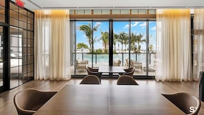 A modern hotel room with a large window, a balcony with outdoor seating, and a view of palm trees and a building. - Chic & Cozy Downtown Miami Studio | City Views (Miami)