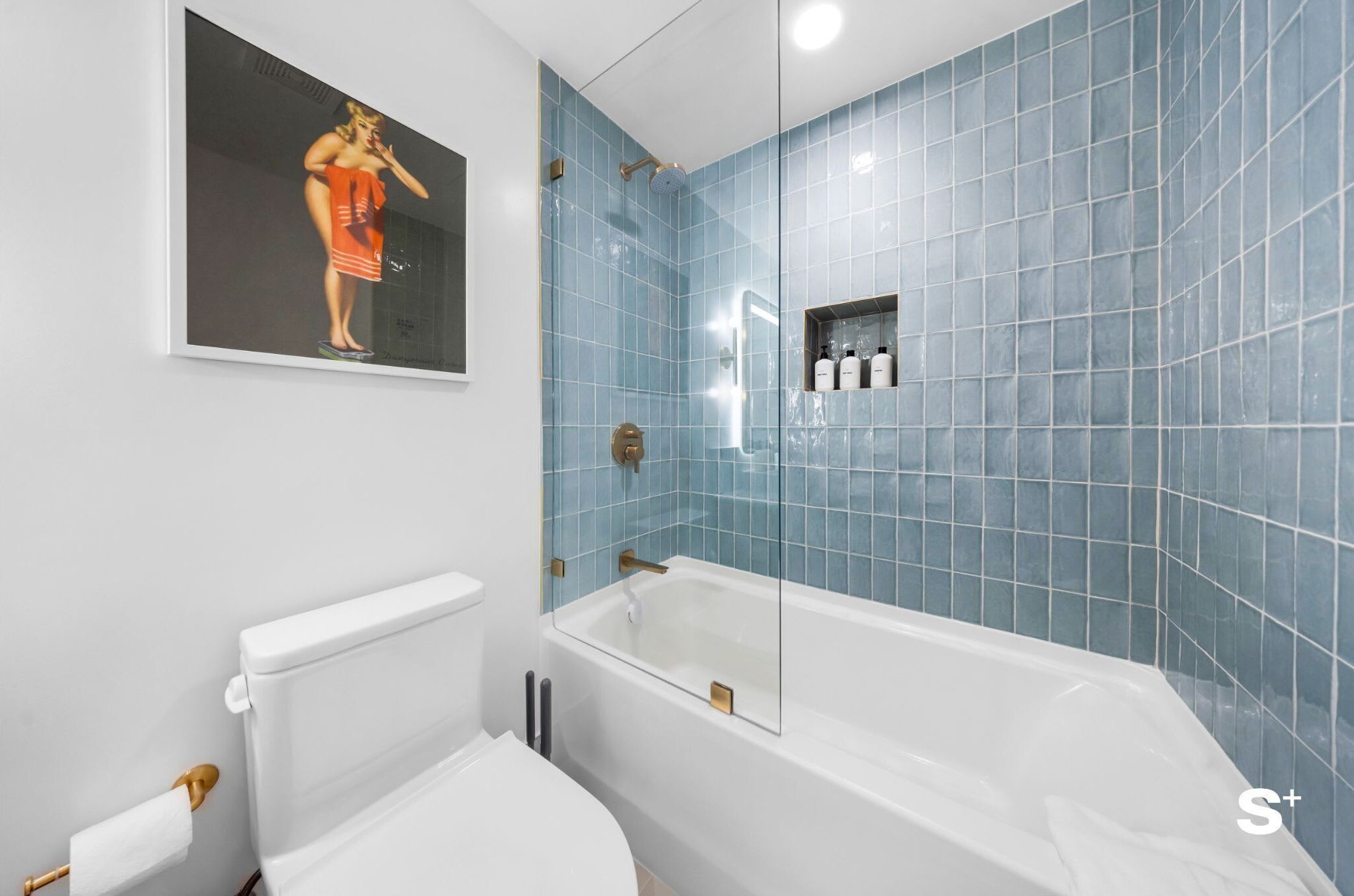 A bathroom with a white toilet, a bathtub with a glass enclosure, and blue tiled walls.