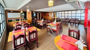 A restaurant with wooden tables and chairs, a chandelier, and large windows. - HOTEL MANGALA TEMPLE VIEW (Chavakkad)