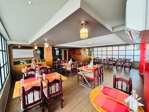 A restaurant with wooden tables and chairs, a chandelier, and large windows. - HOTEL MANGALA TEMPLE VIEW (Chavakkad)