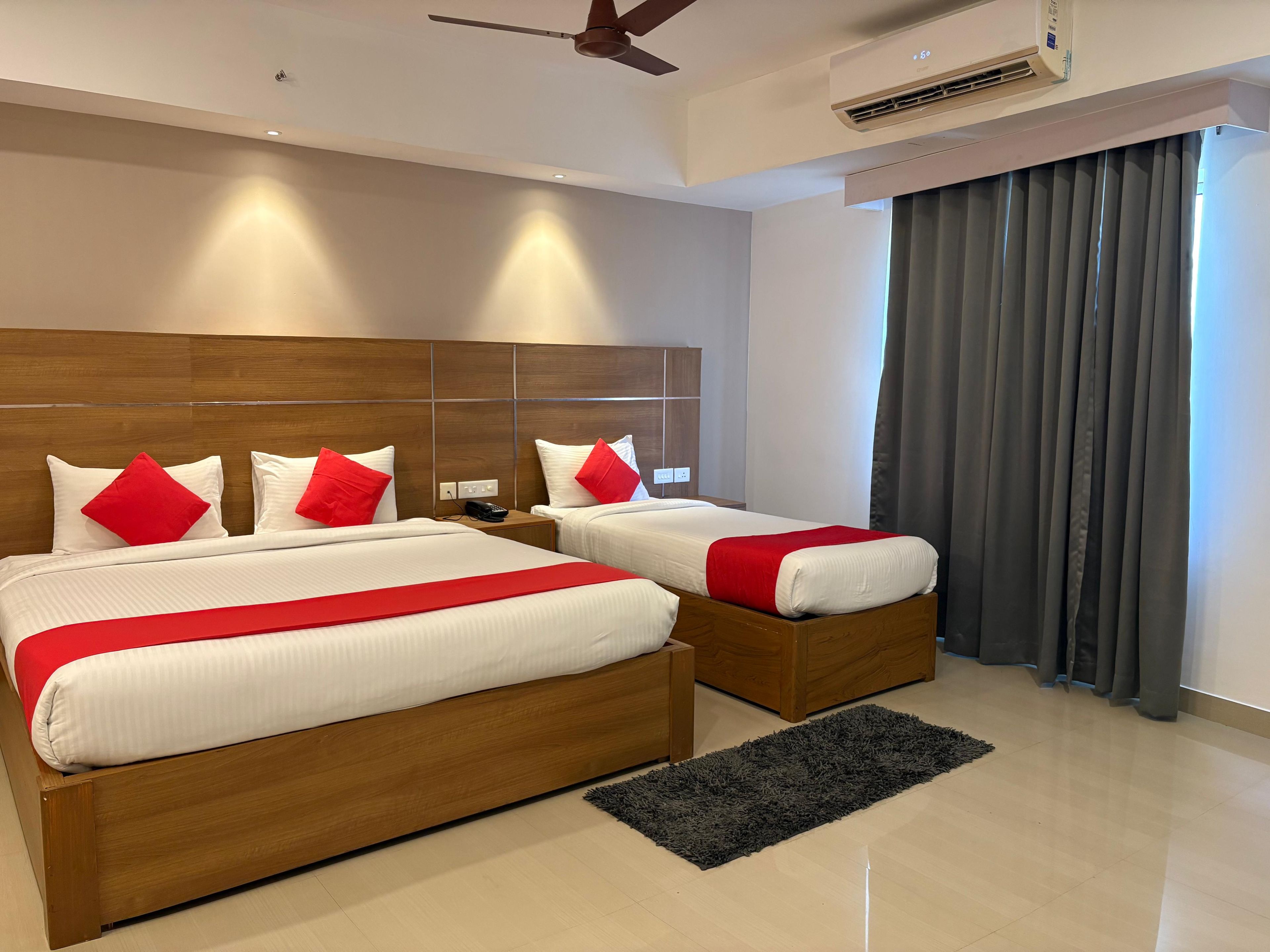 Habitación de hotel con dos camas, cabecero de madera, ventilador de techo, aire acondicionado y vistas al exterior a través de una ventana con cortinas.