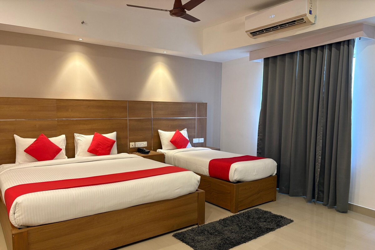 A hotel room with two beds, a wooden headboard, a ceiling fan, an air conditioning unit, and a view of the outside through a window with curtains.