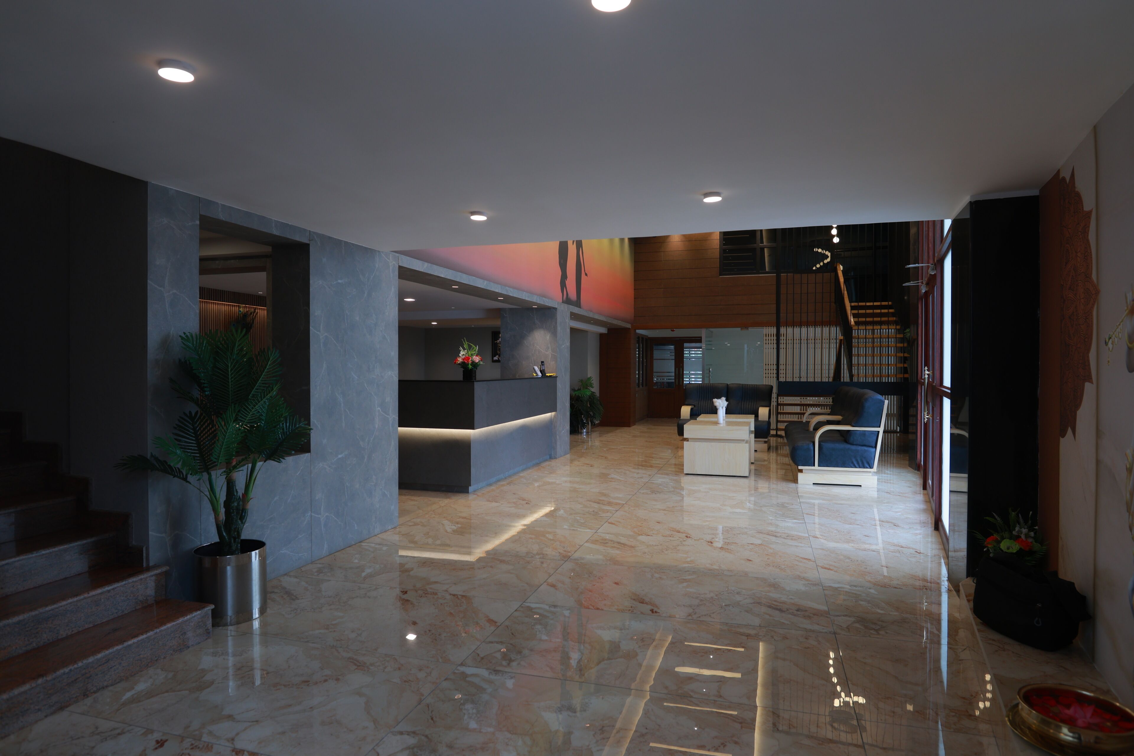 A spacious lobby with a marble floor, a reception desk, a staircase, and seating areas.