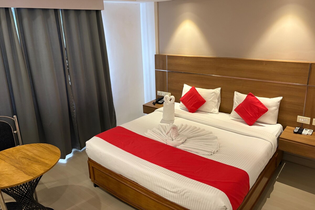 A hotel room with a bed, a wooden nightstand, a table, and a chair.