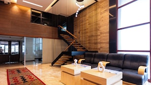 A modern interior with a staircase, a black leather sofa, and wooden coffee tables. - HOTEL MANGALA TEMPLE VIEW (Chavakkad)