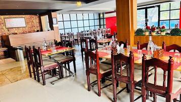 A restaurant with wooden chairs and tables, a bar area, and large windows.