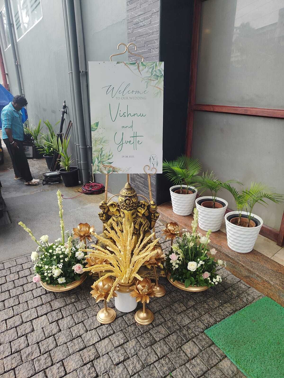 A wedding welcome sign, potted plants, and a decorative golden structure.