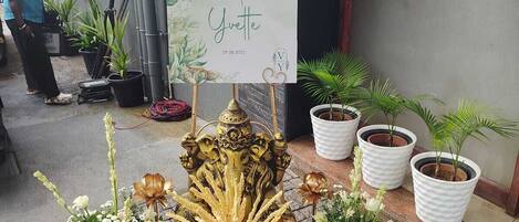 Un letrero de bienvenida de boda, plantas en macetas y una estructura dorada decorativa.