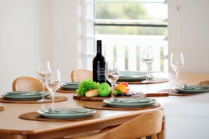 Une table à manger dressée avec des assiettes, des couverts et une bouteille de vin, avec une fenêtre en arrière-plan.