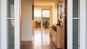 A hallway leading to a balcony with wicker chairs, a wooden counter, and a view of the outdoors. - “Sunrise & Sunset” – Panoramic Ocean Views (Copacabana)