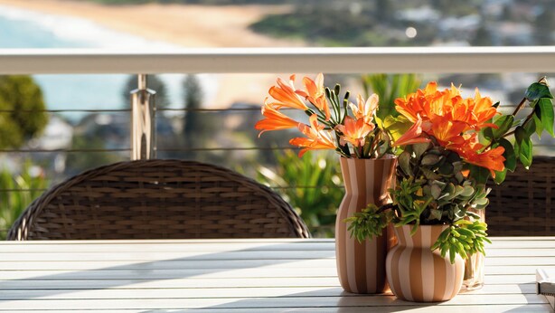 A balcony with wicker chairs and two striped vases with orange flowers. - “Sunrise & Sunset” – Panoramic Ocean Views (Copacabana)
