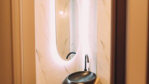 Un baño con lavamanos de mármol y espejo con marco iluminado.