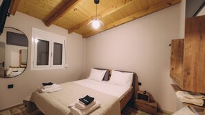 Un dormitorio con techo de madera, una cama con ropa de cama blanca, una mesita de noche, un espejo y un armario de madera.