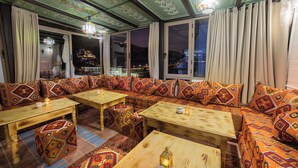 Ein gemütliches Interieur mit gemusterten Sofas und Holztischen, großen Fenstern mit Vorhängen und dekorativer Beleuchtung.