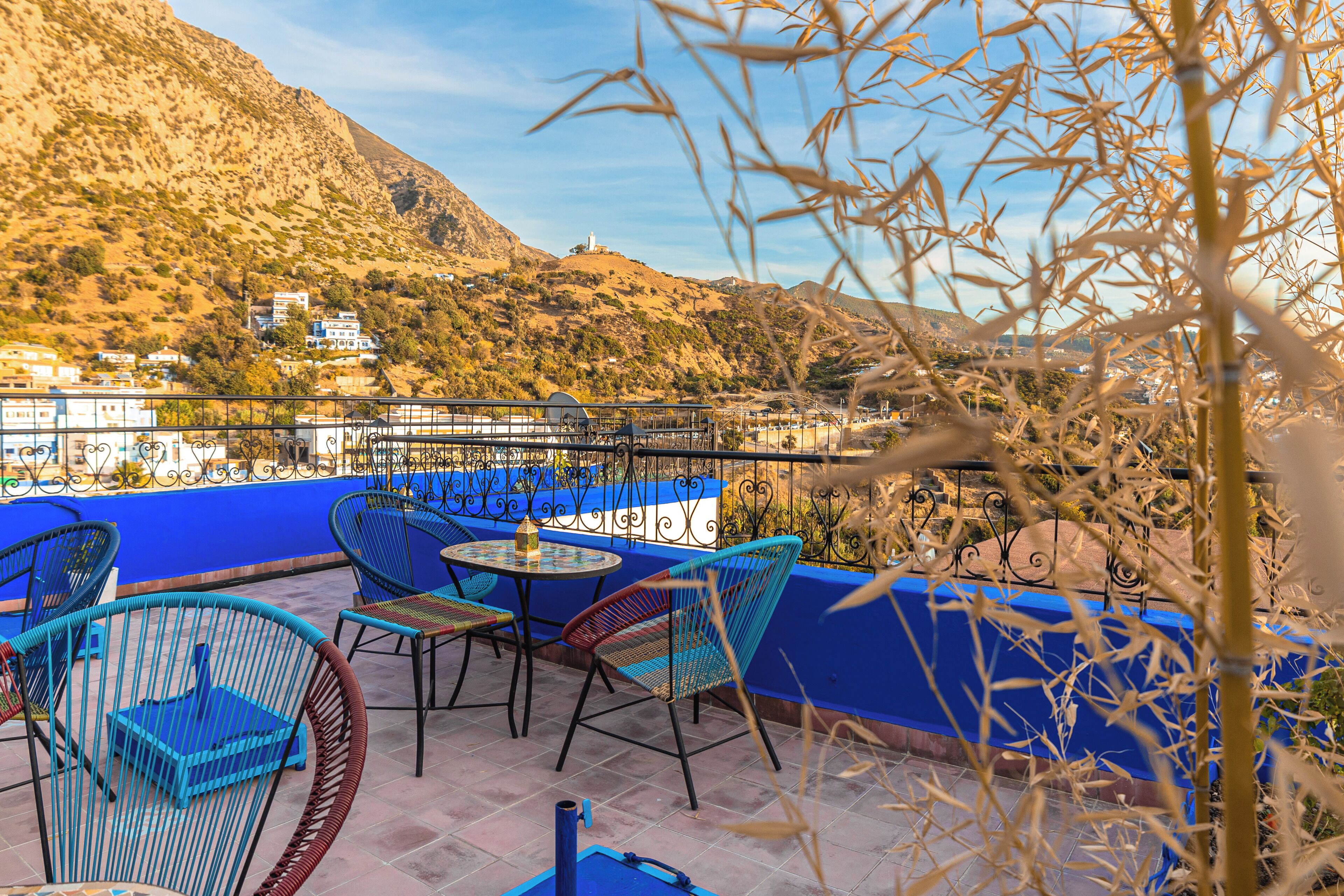 Una terraza con barandillas azules, sillas de mimbre y una mesa con una botella.