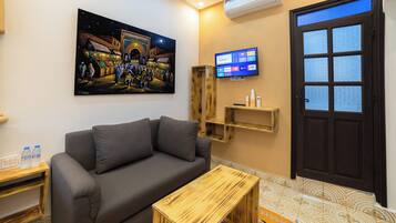 Una sala de estar con un sofá, una mesa de centro de madera, un cuadro, un televisor y una puerta con paneles de vidrio esmerilado.
